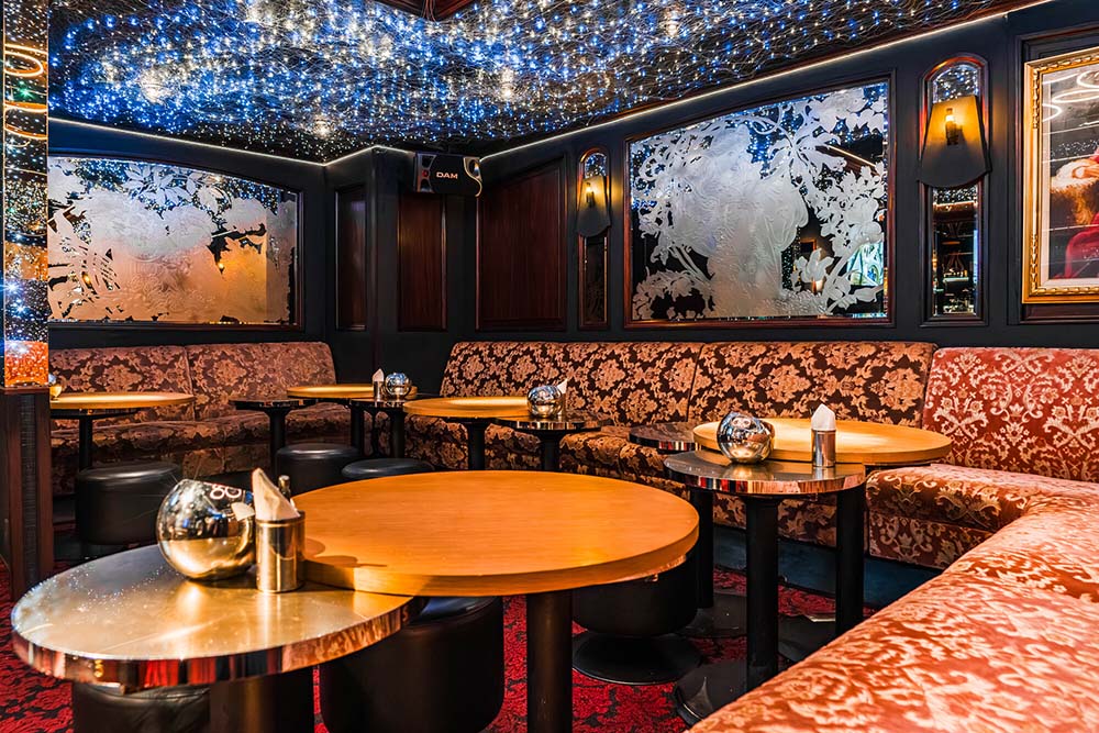Elegant lounge with ornate floral upholstery, round tables, and a ceiling decorated with blue and white twinkling lights.